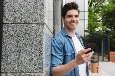 Mutlu genç inanılmaz adam işadamı cep telefonu kahve içme sohbet yürüyüş dışında açık havada poz.