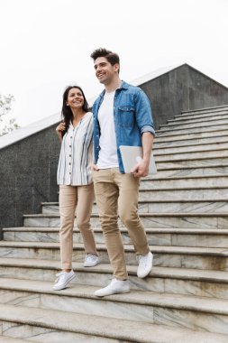 Açık havada merdivenlerden aşağı yürürken gülümseyen ve konuşan neşeli çift görüntü