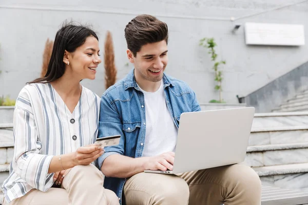 Feliz joven increíble pareja amorosa gente de negocios colegas al aire libre utilizando ordenador portátil con tarjeta de crédito . — Foto de Stock