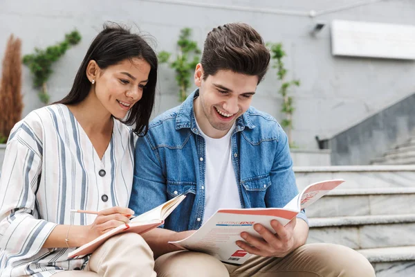 Erstaunliche liebevolle Paar Studenten Kollegen draußen auf Stufen lesen Buch schreiben Notizen studieren. — Stockfoto