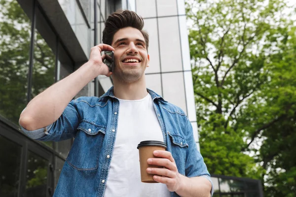 Happy young amazing man businessman posing outdoors outside walking talking by mobile phone drinking coffee. — Stock Photo, Image