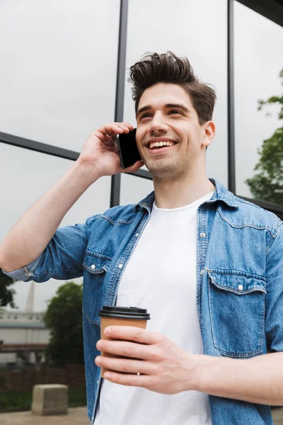 Happy young amazing man businessman posing outdoors outside walking talking by mobile phone drinking coffee. — Stock Photo, Image