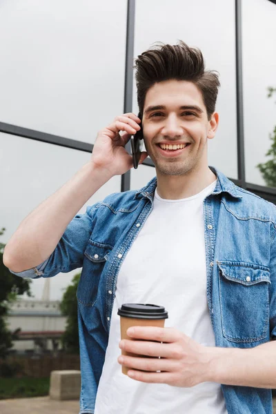 Happy young amazing man businessman posing outdoors outside walking talking by mobile phone drinking coffee. — Stock Photo, Image