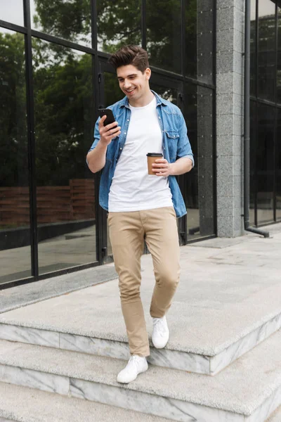 Boldog fiatal csodálatos férfi üzletember pózol a szabadban kívül gyaloglás beszélgető mellett mozgatható telefon ivás kávé. — Stock Fotó