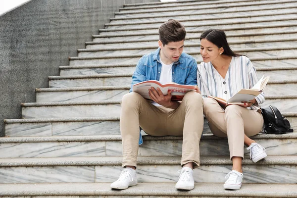 Amazing loving couple students colleagues outdoors outside on steps reading book writing notes studying.