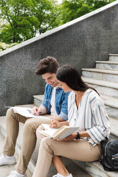 Amazing loving couple students colleagues outdoors outside on steps reading book writing notes studying.