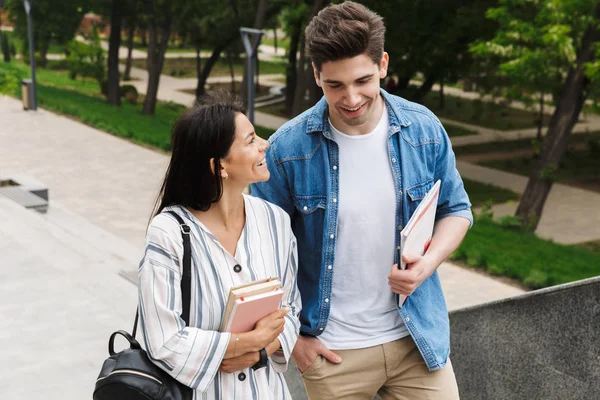 Incroyable couple d'étudiants aimants à l'extérieur marchant par étapes avec des livres . — Photo