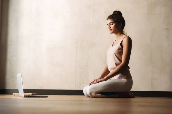 Foto av fokuserad lugn kvinna i sportkläder mediterar med slutna ögon när du sitter på golvet — Stockfoto