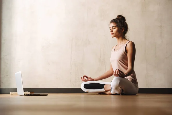 Foto av koncentrerad attraktiv kvinna mediterar med Zen fingrar och använda laptop medan du sitter på golvet hemma — Stockfoto
