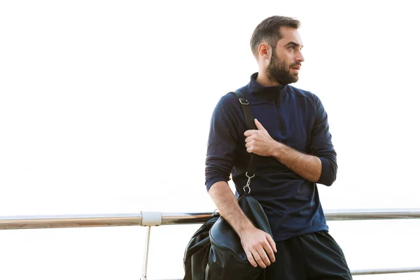 Guapo joven deportista en forma llevando bolsa de pie — Foto de Stock