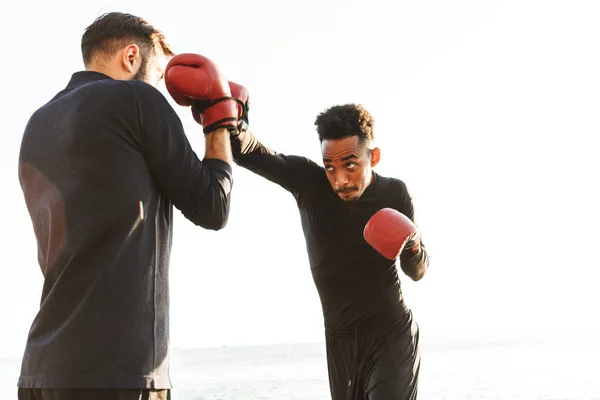 Serious handsome strong two young sports men boxers friends at the beach near sea boxing. — Stock Photo, Image