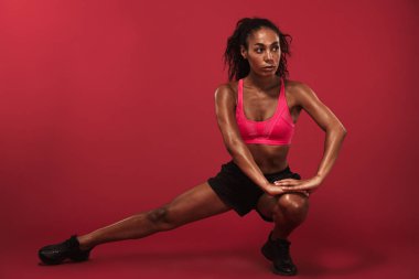 Konsantre güçlü genç afrikalı spor kadın kırmızı duvar arka plan üzerinde izole poz spor egzersizleri yapmak.
