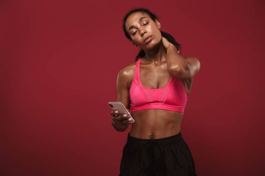 Güçlü genç afrika fitness spor kadın cep telefonu sohbet kullanarak kırmızı duvar arka plan üzerinde izole poz.