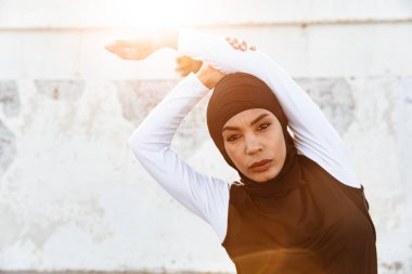 Hicap ve koyu giysiler poz giymiş Konsantre Müslüman spor fitness kadın sokakta açık havada spor germe egzersizleri yapmak.