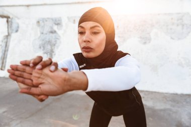 Güçlü müslüman spor fitness kadın başörtüsü ve koyu giysiler poz giymiş spor germe egzersizleri sokakta açık havada yapmak.