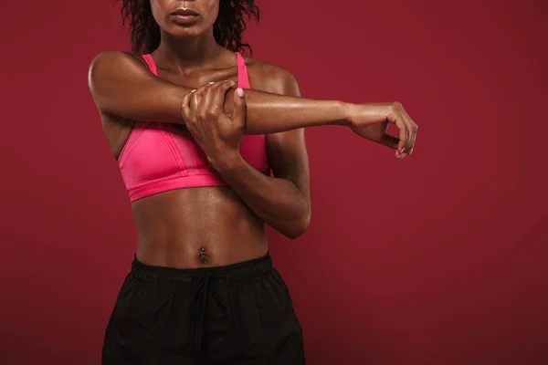 Concentrado forte jovem Africano fitness esportes mulher posando isolado sobre fundo de parede vermelha fazer exercícios de alongamento . — Fotografia de Stock
