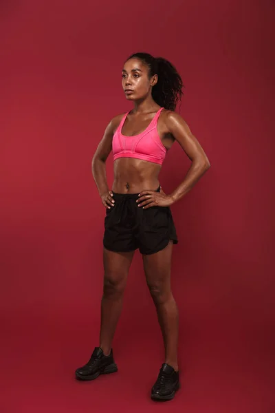 Strong young african fitness sports woman posing isolated over red wall background. — Stock Photo, Image