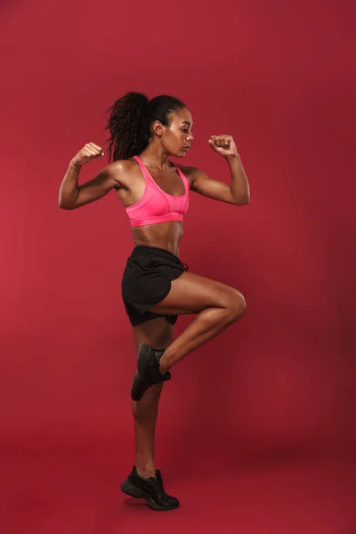 Konzentriert starke junge afrikanische Sportlerin posiert isoliert über roter Wand Hintergrund machen Sport-Übungen. — Stockfoto