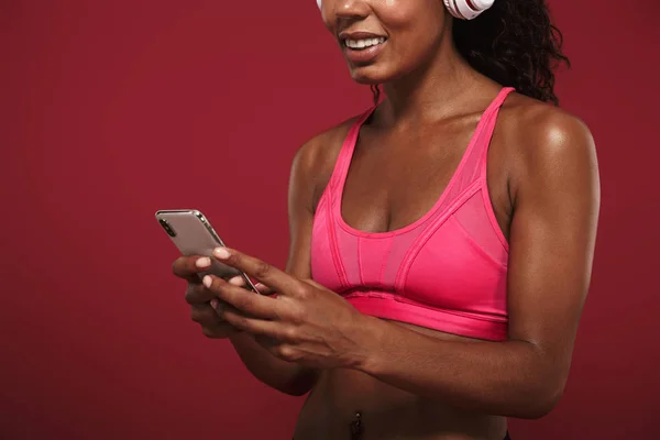 미소 기쁘게 강한 젊은 아프리카 피트 니스 스포츠 여자 헤드폰으로 빨간 벽 배경 듣기 음악을 통해 고립 된 포즈. — 스톡 사진