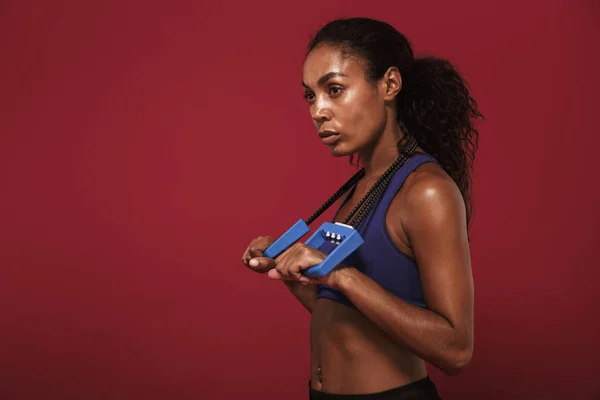 Ernste starke junge afrikanische Fitness-Sportlerin posiert isoliert über roter Wand Hintergrund posiert mit Expander. — Stockfoto