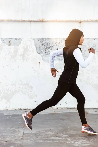 Muslim concentrado deporte fitness mujer vestida con hijab y ropa oscura corriendo al aire libre . — Foto de Stock