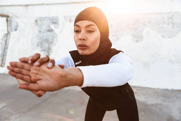 Silna muzułmańska sportowa fitness kobieta ubrana w hidżab i ciemne ubrania stwarzające sprawiają, że ćwiczenia rozciągające Sport na zewnątrz na ulicy. — Zdjęcie stockowe