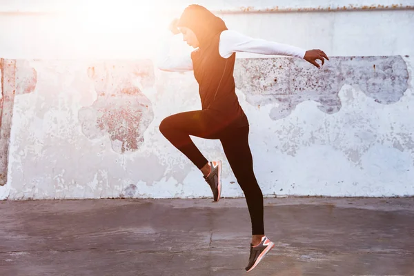 Συγκεντρωμένη μουσουλμανική αθλητική γυμναστική γυναίκα ντυμένη σε χιτζάμπ και σκούρα ρούχα που θέτουν κάνει άθλημα τέντωμα ασκήσεις σε εξωτερικούς χώρους στο δρόμο τρέξιμο. — Φωτογραφία Αρχείου