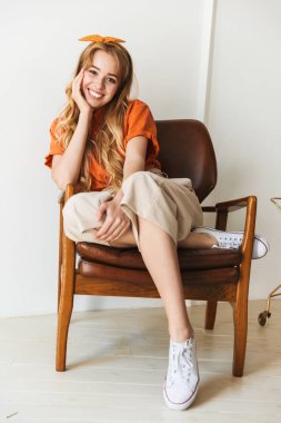 Sevimli mutlu iyimser gülümseyen genç sarışın kız evde kapalı sandalyede oturan poz.