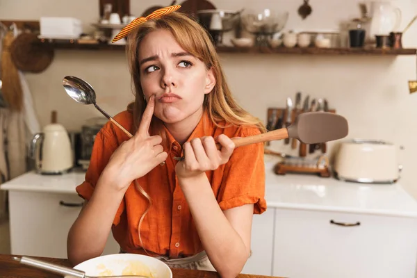 Trist blond kokk som lager mat på kjøkkenet og tenker: . – stockfoto