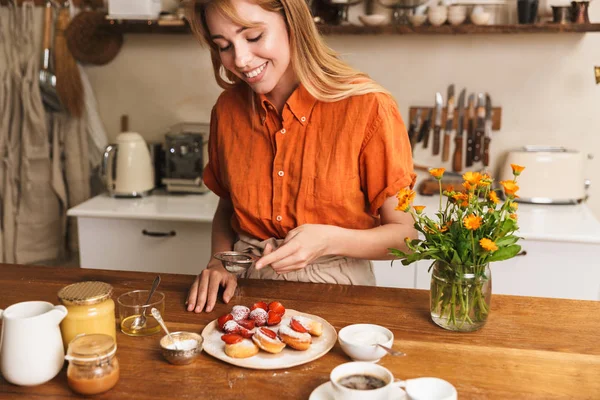 Blij glimlachend vrolijk jong blond meisje chef-kok koken in de keuken aardbei zoete gebak. — Stockfoto