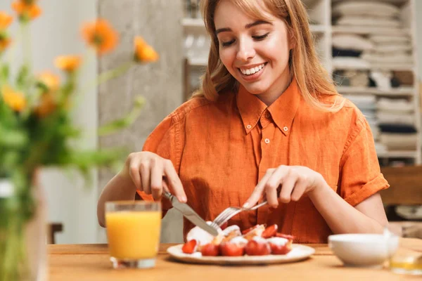 Feliz jovem loira menina no o cozinha comer doce pastelaria ter um pequeno-almoço beber suco . — Fotografia de Stock