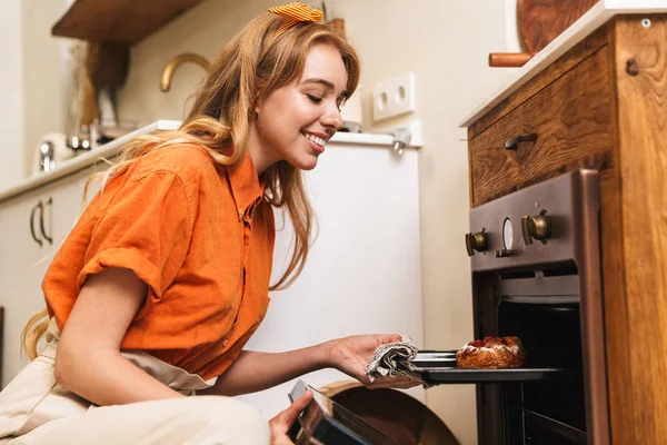 Mosolygó fiatal szőke lány séf a konyhában főzés édes tészta. — Stock Fotó