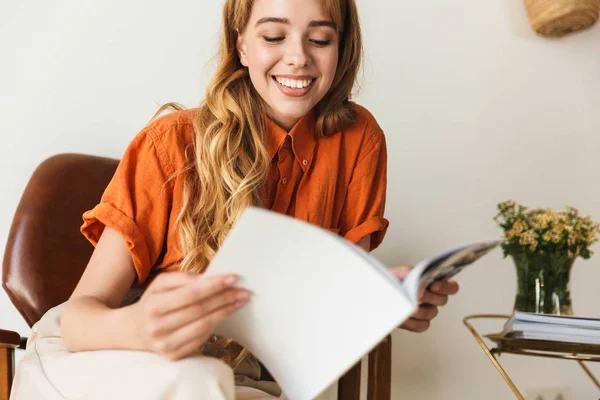 Souriant jeune fille blonde à la maison intérieur lecture magazine . — Photo