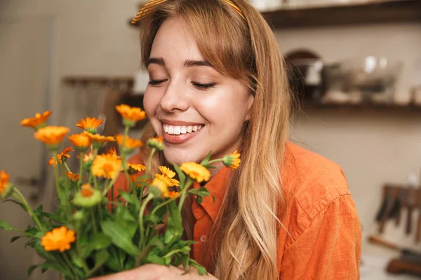 手に美しい花を持つ台所で陽気な笑顔若いブロンドの女の子. — ストック写真
