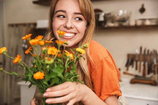 Alegre sorrindo jovem loira na cozinha segurando belas flores nas mãos . — Fotografia de Stock