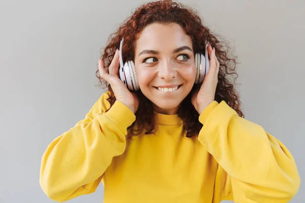 Feliz hermosa chica rizada aislado sobre fondo gris escuchar música con auriculares . — Foto de Stock