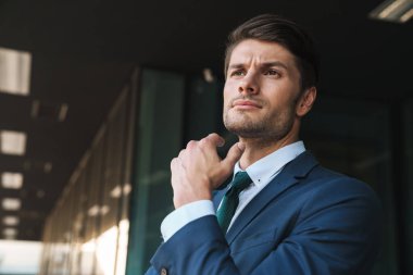 Kendine güvenen işadamının ayaktayken çenesine dokunduğu fotoğraf 