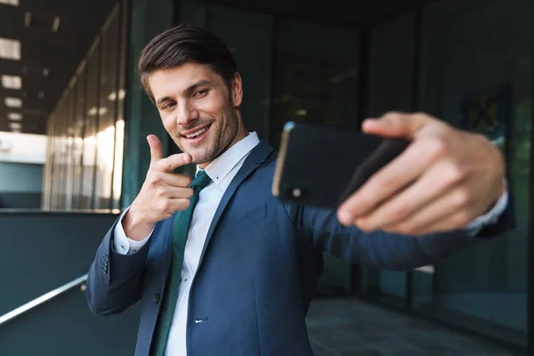 Optimistic young business man outdoors at the street near business center take selfie by mobile phone. — Stock Photo, Image