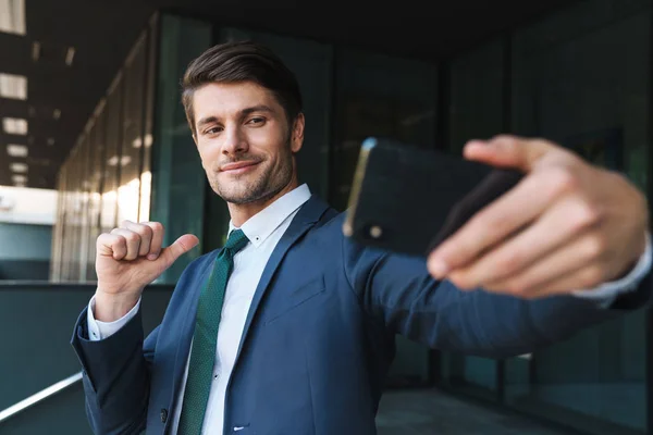 Joven hombre de negocios al aire libre en la calle cerca del centro de negocios tomar selfie por teléfono móvil . — Foto de Stock