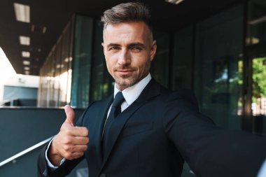 Olgun gri saçlı yakışıklı iş adamı iş merkezi yakınındaki sokakta açık havada kamera ile selfie çekmek.