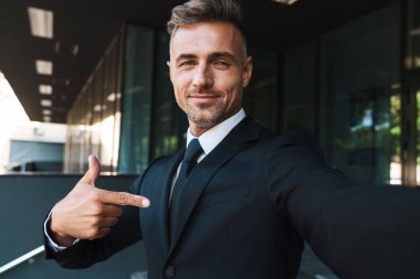 Memnun pozitif olgun gri saçlı yakışıklı iş adamı iş merkezi yakınındaki sokakta açık kamera ile selfie çekmek.