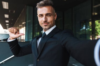 Memnun pozitif olgun gri saçlı yakışıklı iş adamı iş merkezi yakınındaki sokakta açık kamera ile selfie çekmek.