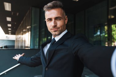 Memnun pozitif olgun gri saçlı yakışıklı iş adamı iş merkezi yakınındaki sokakta açık kamera ile selfie çekmek.