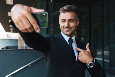 Gülşen mutlu olgun gri saçlı iş adamı iş merkezi yakınındaki sokakta açık havada kendini işaret cep telefonu ile selfie çekmek.