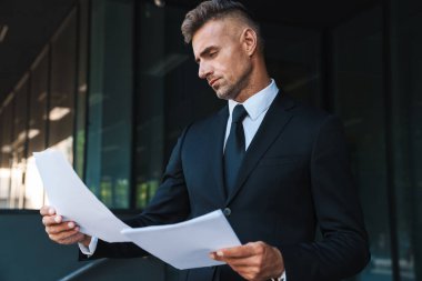 Ciddi olgun yakışıklı gri saçlı iş adamı iş merkezi yakınında sokakta açık gazete okuma.