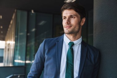 Konsantre ciddi genç tıraşsız yakışıklı iş adamı iş merkezi yakınında sokakta bir kenara bakarak poz.