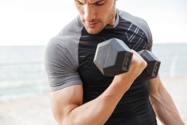 Deniz kenarında ahşap iskele üzerinde çalışırken dambıl ile egzersiz yapan eşofman yakışıklı adam Fotoğrafı