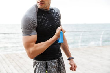 Deniz kenarında ahşap iskele üzerinde çalışırken genişletici ile egzersiz yapan eşofmanlı kafkas adamın fotoğrafı kırpılmış