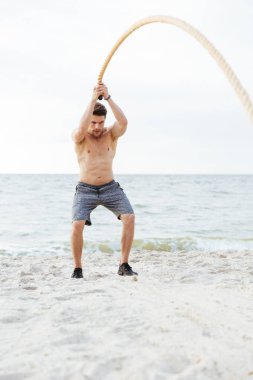 Deniz kenarında sahilde fitness ipi ile çalışan sportif yarı çıplak adam Fotoğrafı