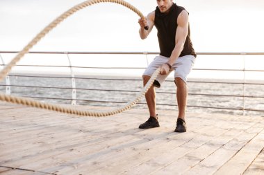 Sahildeki ahşap iskelede fitness ipi ile çalışan eşofmanlı genç adamın fotoğrafı